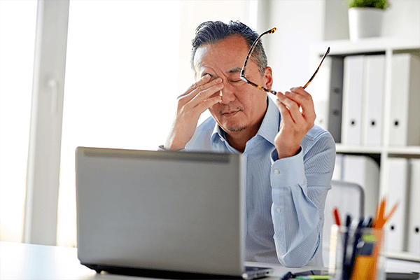 Man tired looking at a computer with glasses in his hand